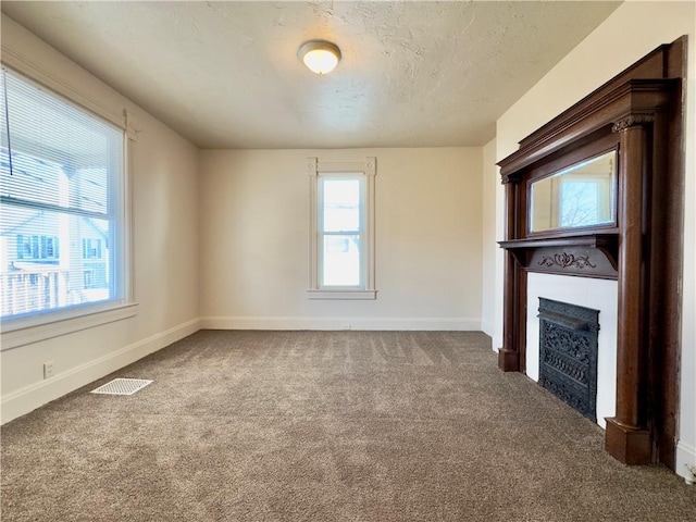 unfurnished living room featuring a textured ceiling, carpet floors, a fireplace, visible vents, and baseboards