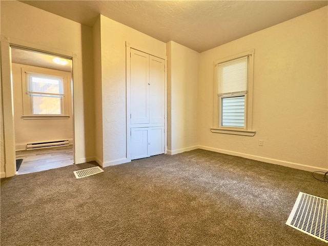 unfurnished bedroom with baseboards, visible vents, dark colored carpet, a baseboard heating unit, and a closet