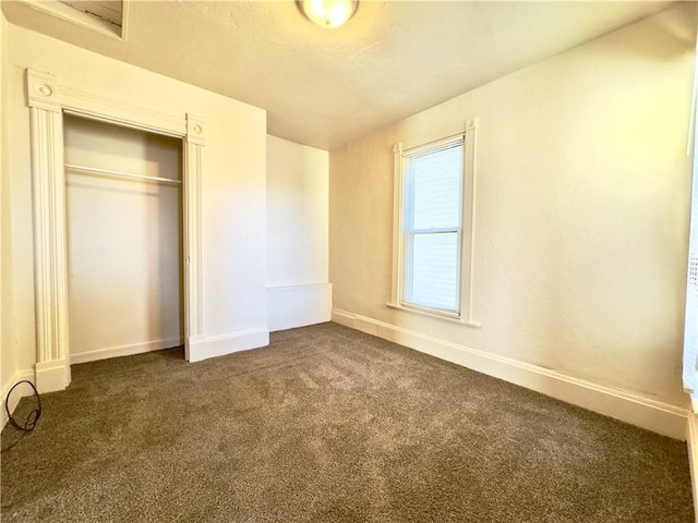 unfurnished bedroom with dark colored carpet, a closet, and baseboards