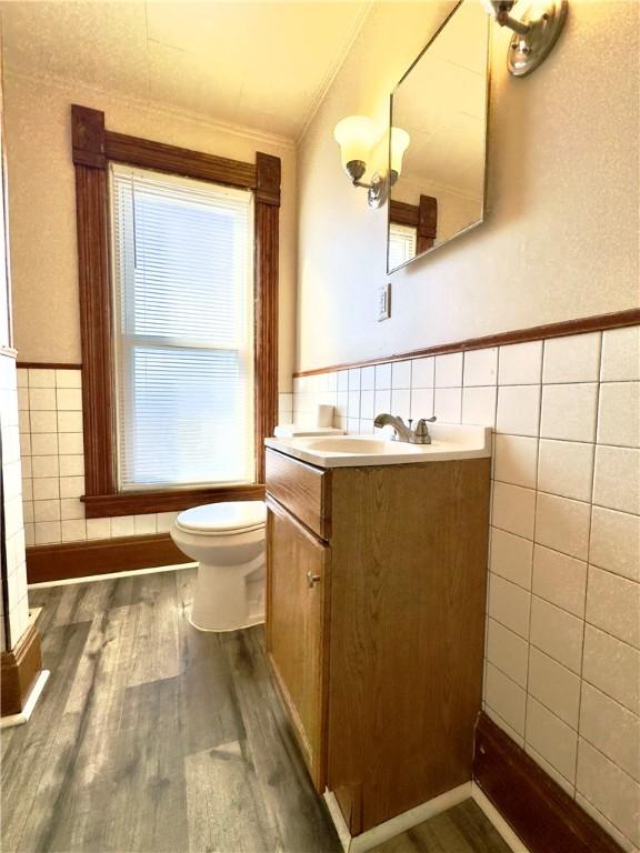 bathroom featuring toilet, wood finished floors, vanity, tile walls, and ornamental molding