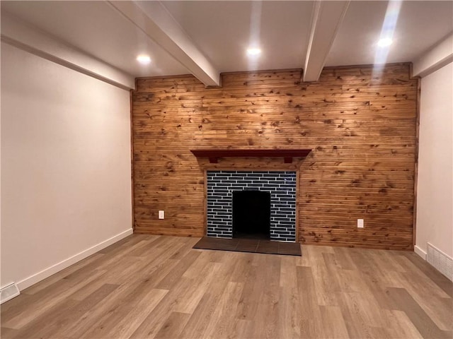 unfurnished living room featuring beam ceiling, light wood-type flooring, and wood walls