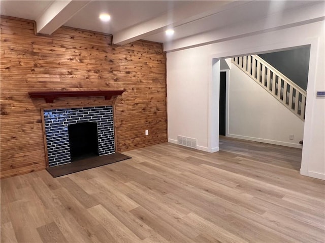 unfurnished living room with wooden walls, beam ceiling, and light hardwood / wood-style floors