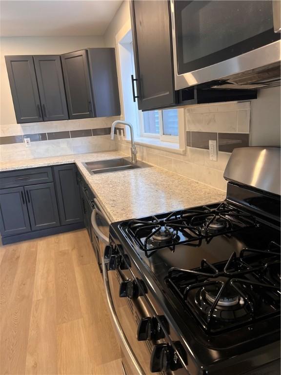 kitchen featuring sink, gas range, backsplash, and light wood-type flooring