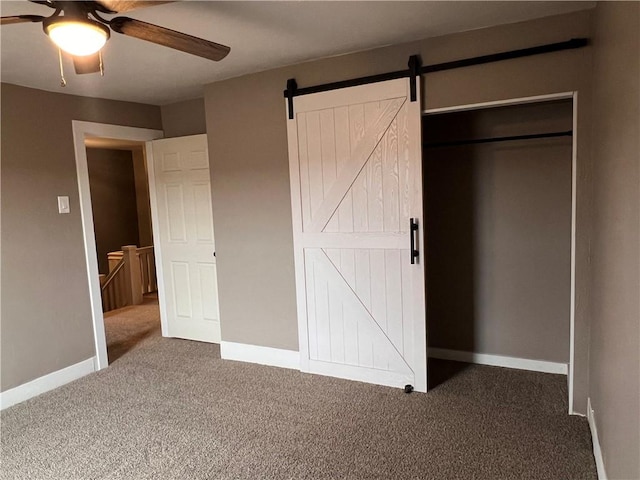 unfurnished bedroom with dark carpet, a barn door, and ceiling fan