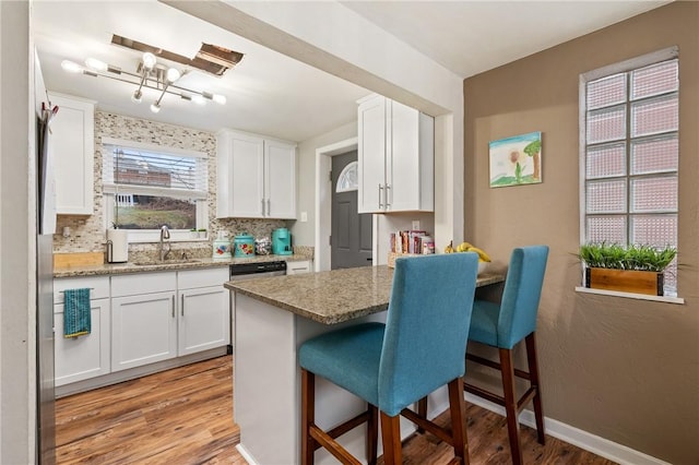 kitchen with a breakfast bar, white cabinetry, decorative backsplash, light stone countertops, and light wood-type flooring