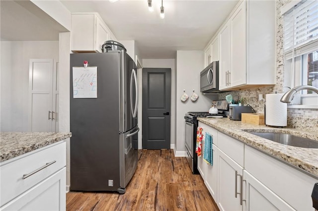 kitchen with sink, light hardwood / wood-style flooring, white cabinetry, stainless steel appliances, and light stone countertops