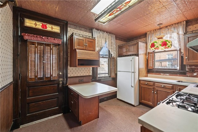 kitchen with sink, wooden walls, extractor fan, light carpet, and white fridge