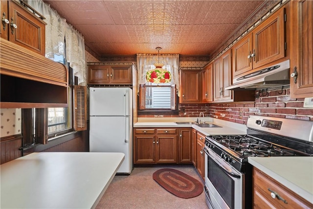 kitchen with sink, hanging light fixtures, white fridge, light colored carpet, and gas range