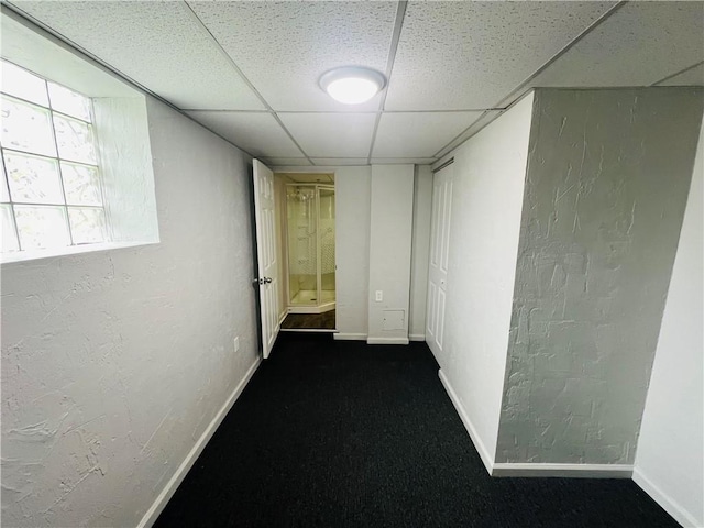 corridor with dark colored carpet and a paneled ceiling