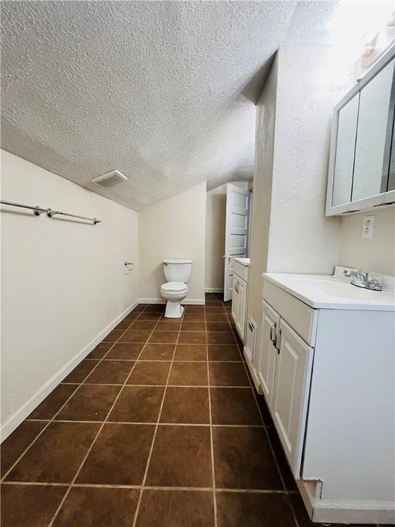 bathroom with lofted ceiling, tile patterned floors, toilet, a textured ceiling, and vanity