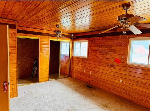 unfurnished bedroom featuring two closets, wooden ceiling, light colored carpet, and wood walls