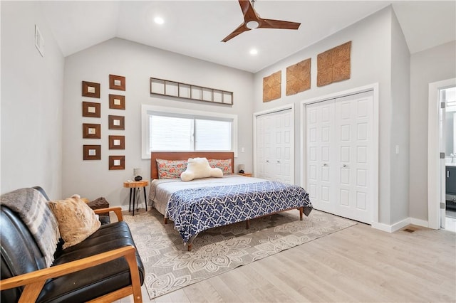 bedroom featuring lofted ceiling, light hardwood / wood-style flooring, ceiling fan, ensuite bathroom, and two closets