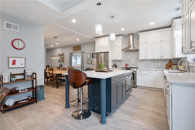 kitchen featuring wall chimney exhaust hood, sink, white cabinetry, a kitchen island, and stainless steel appliances