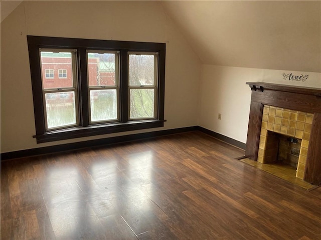 unfurnished living room with lofted ceiling, a tiled fireplace, and dark wood-type flooring