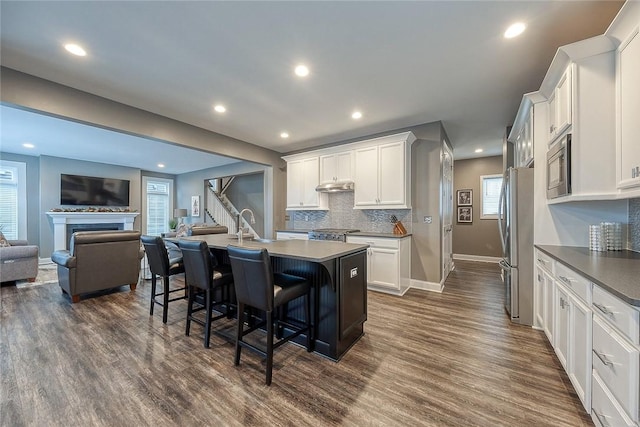 kitchen with white cabinetry, a breakfast bar area, a kitchen island with sink, stainless steel appliances, and dark wood-type flooring