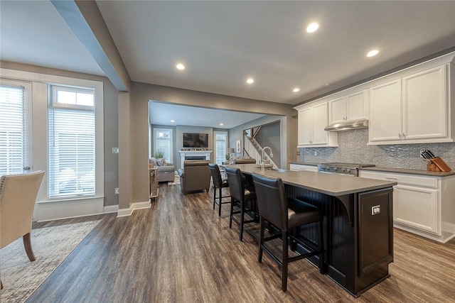 kitchen with white cabinetry, a kitchen bar, dark hardwood / wood-style floors, and an island with sink