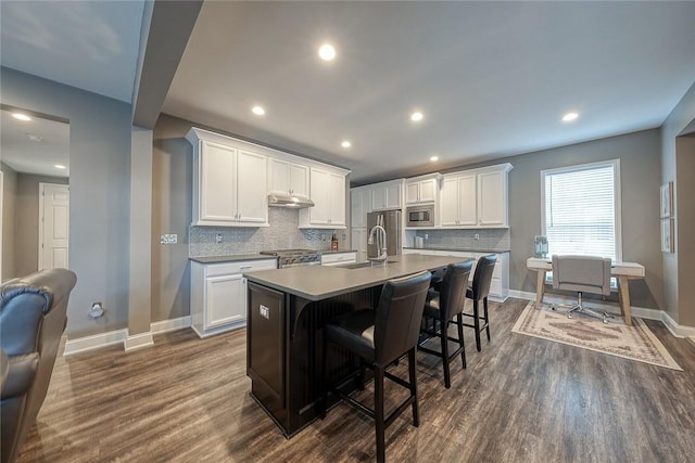 kitchen with a breakfast bar, white cabinetry, dark hardwood / wood-style floors, an island with sink, and stainless steel appliances