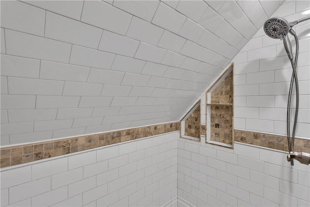 bathroom featuring lofted ceiling, a tile shower, and tile walls