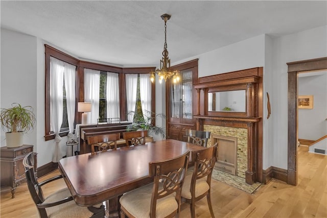 dining area featuring a tile fireplace, an inviting chandelier, and light wood-type flooring