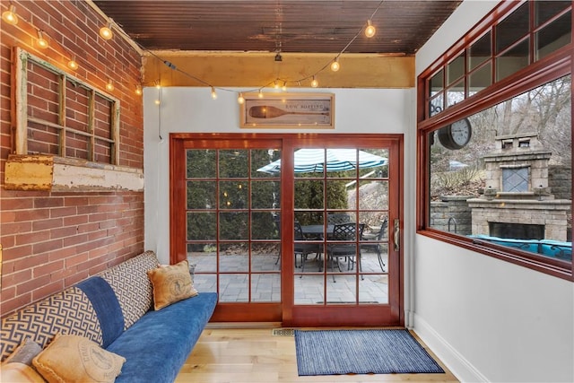 doorway to outside featuring hardwood / wood-style flooring, a fireplace, wooden ceiling, and brick wall