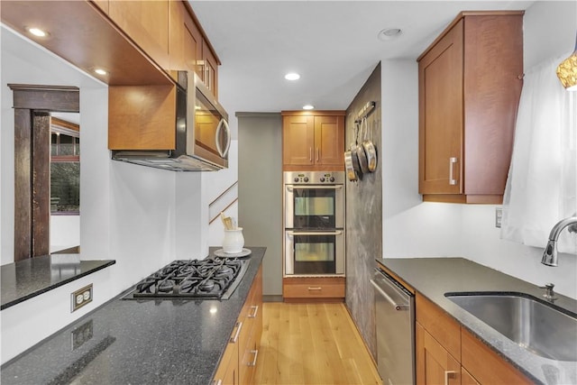 kitchen with sink, light hardwood / wood-style floors, dark stone counters, and appliances with stainless steel finishes