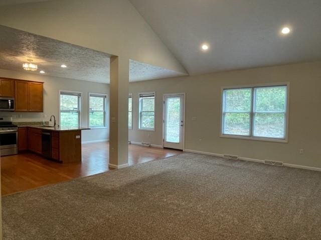 kitchen with sink, high vaulted ceiling, appliances with stainless steel finishes, kitchen peninsula, and light colored carpet