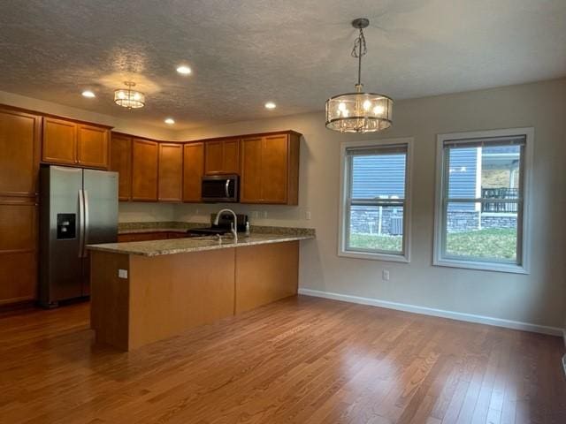 kitchen featuring pendant lighting, appliances with stainless steel finishes, wood-type flooring, light stone countertops, and kitchen peninsula