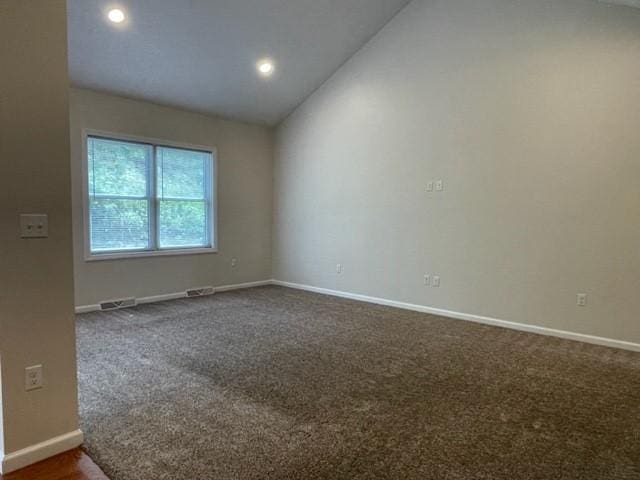 spare room featuring dark colored carpet and lofted ceiling