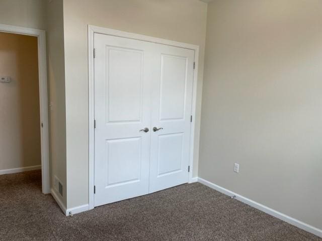 unfurnished bedroom with dark carpet and a closet