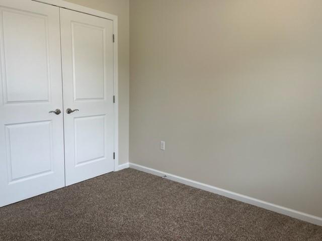 unfurnished bedroom with dark carpet and a closet