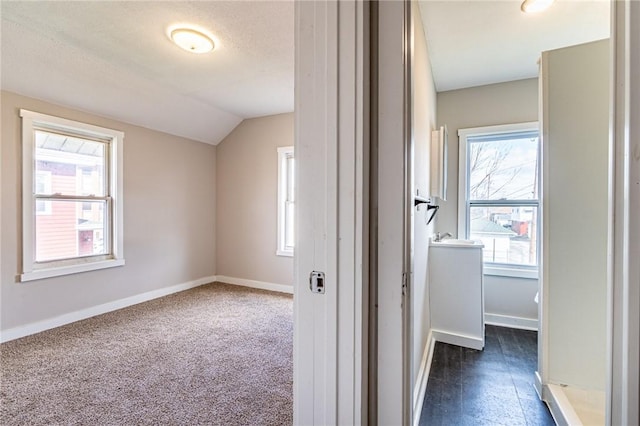 hallway with dark carpet and vaulted ceiling