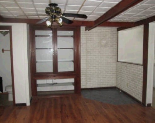 unfurnished dining area featuring brick wall, dark hardwood / wood-style floors, and a paneled ceiling