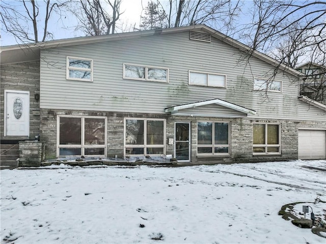 snow covered back of property featuring a garage