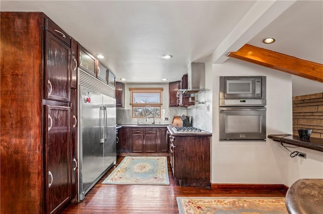 kitchen featuring sink, dark wood-type flooring, beam ceiling, built in appliances, and wall chimney exhaust hood