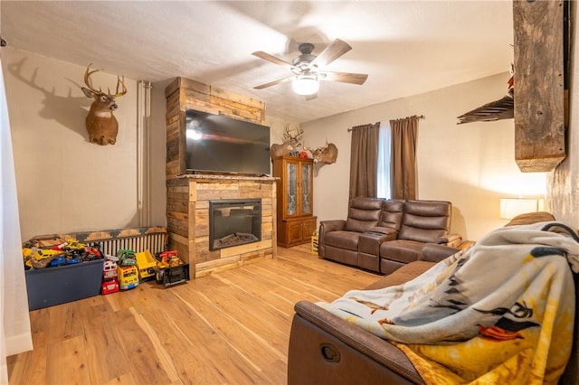 living room featuring ceiling fan, a fireplace, and light wood-type flooring