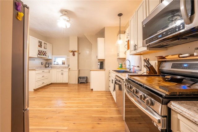 kitchen with decorative light fixtures, sink, white cabinets, stainless steel appliances, and light hardwood / wood-style flooring