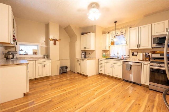 kitchen with sink, white cabinetry, light wood-type flooring, pendant lighting, and stainless steel appliances