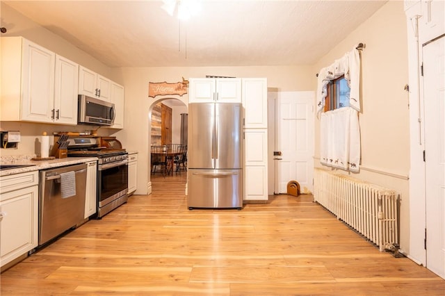 kitchen with radiator heating unit, stainless steel appliances, light hardwood / wood-style floors, and white cabinets