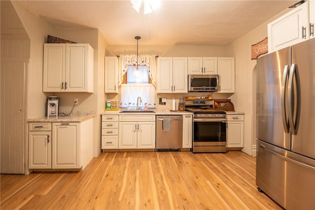 kitchen with sink, white cabinetry, stainless steel appliances, decorative light fixtures, and light wood-type flooring