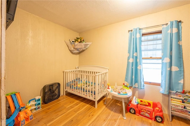 bedroom featuring a nursery area, wood-type flooring, and a textured ceiling