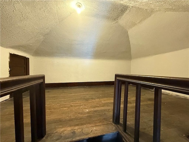 bonus room with dark wood-type flooring, lofted ceiling, and a textured ceiling