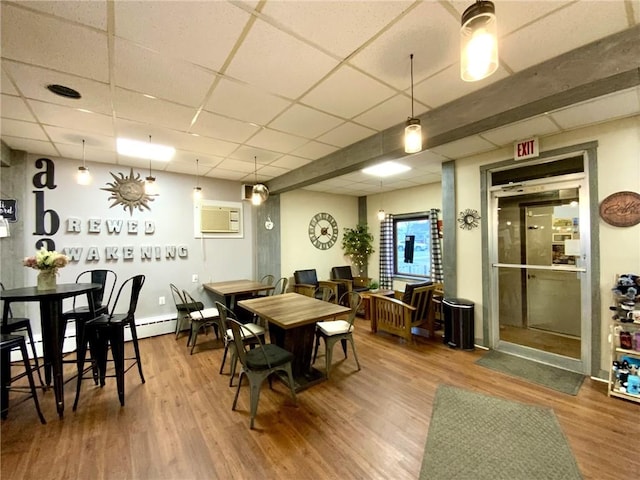 dining area featuring wood-type flooring, an AC wall unit, and a paneled ceiling