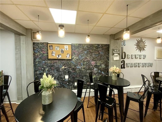 dining space with hardwood / wood-style floors, a paneled ceiling, and a baseboard radiator