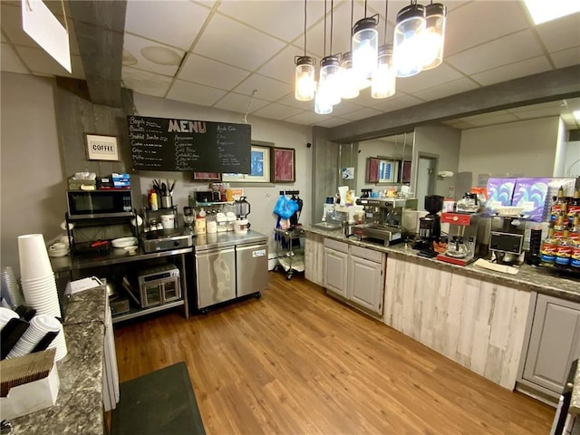 kitchen featuring hanging light fixtures, dark stone countertops, a paneled ceiling, and light wood-type flooring