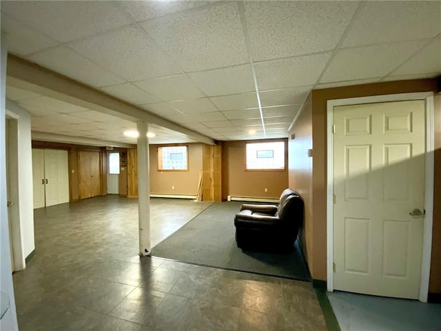 basement featuring a paneled ceiling and baseboard heating