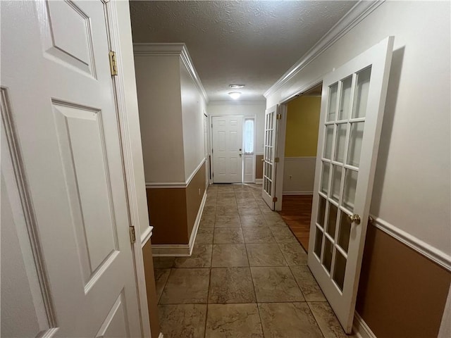 hallway with tile patterned floors, ornamental molding, french doors, and a textured ceiling