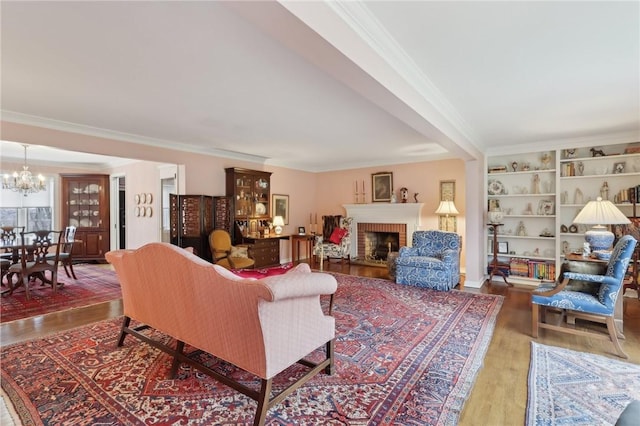 living room featuring wood-type flooring, ornamental molding, a notable chandelier, and a fireplace