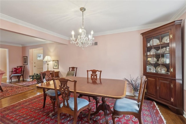 dining area with dark wood-type flooring, crown molding, and a chandelier