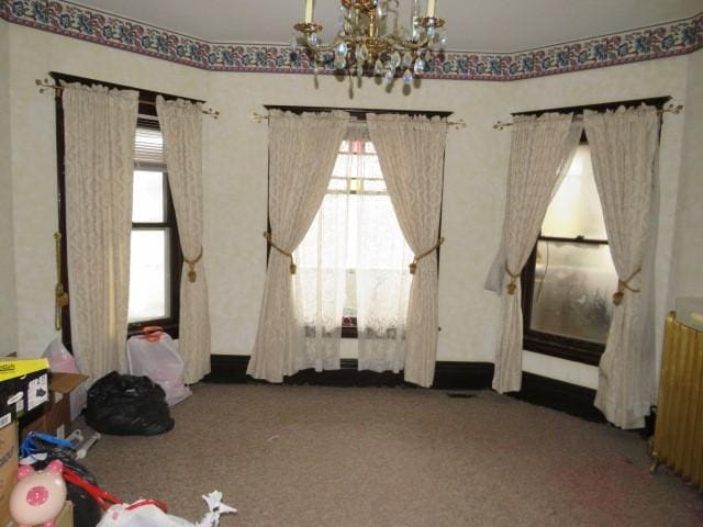 unfurnished bedroom featuring radiator heating unit, a chandelier, carpet, and multiple windows