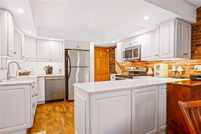 kitchen featuring white cabinetry, stainless steel appliances, kitchen peninsula, and a raised ceiling